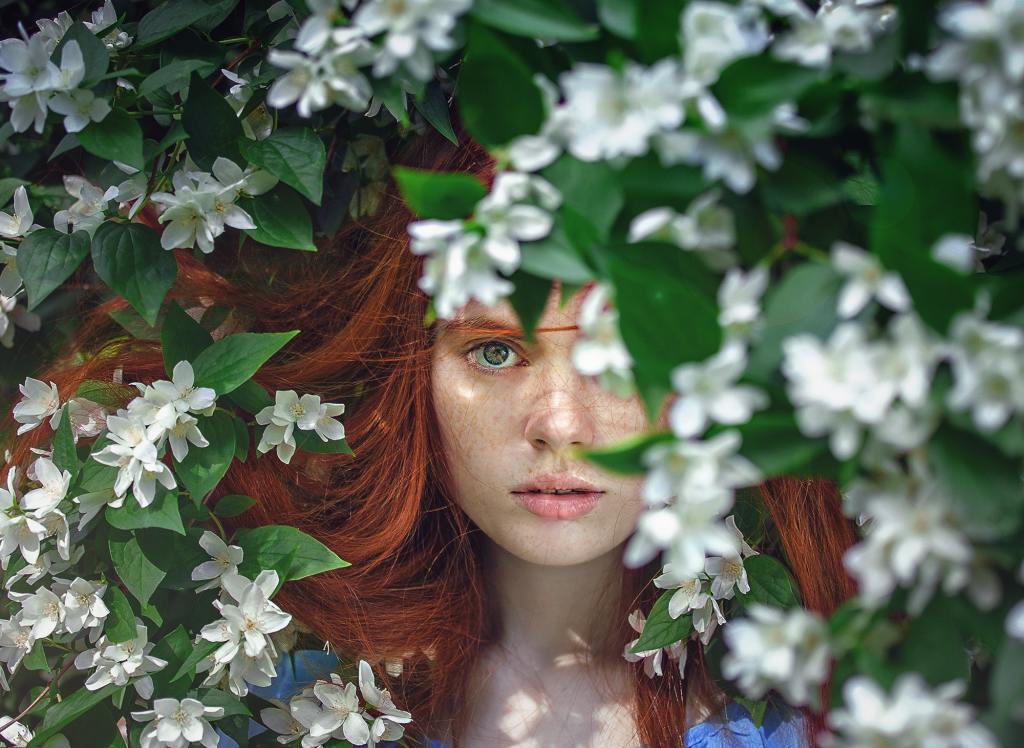 A freckled, red haired girl lies amidst apple blossoms and stares intensely at the camera